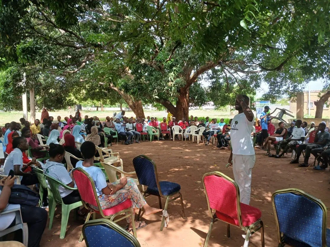 A HERI facilitator leads a community education forum under a large shade tree in Diani
