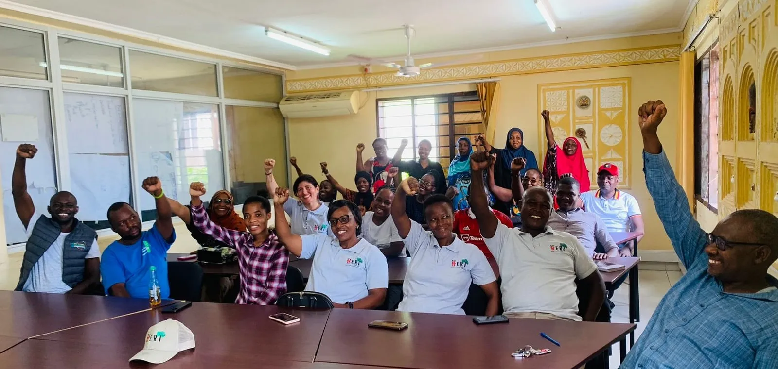 Smiling HERI-Kenya members and community partners raise their fists together in celebration